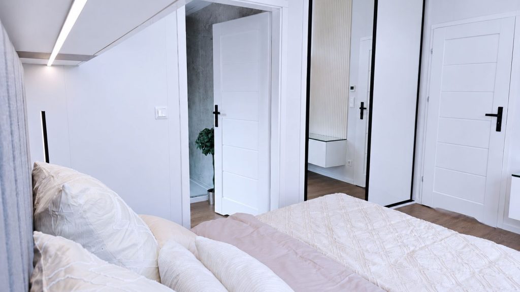 Schlafzimmer mit Spiegelschrank, weißen Türen und Blick ins Bad im Modulhaus - Lieferung nach Krems.