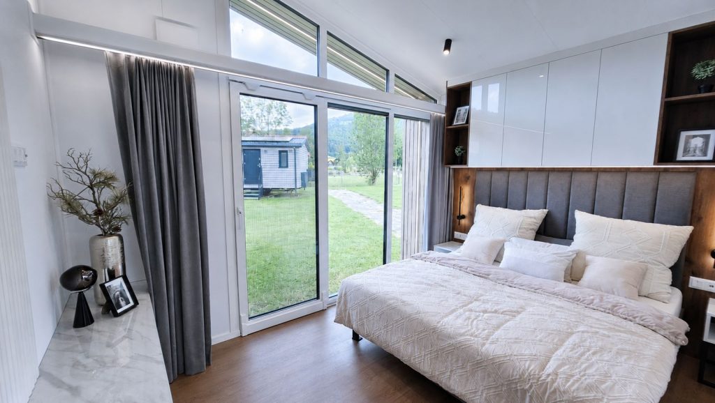 Schlafbereich mit hohem Giebelfenster und Gartenblick, mobiles Eigenheim mit Lieferung nach Vorarlberg.