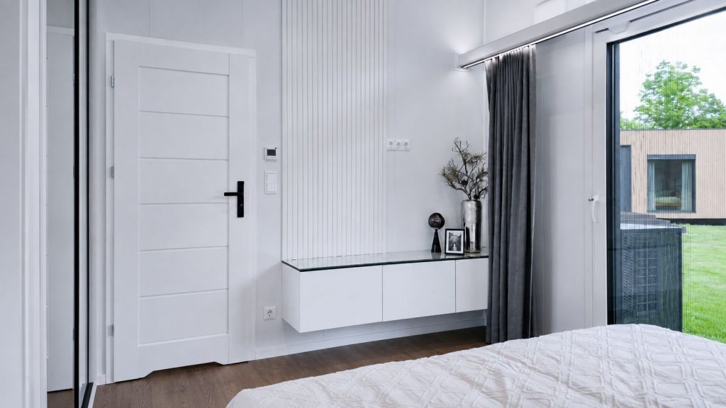 Schlafzimmerecke mit weißer Lamellenwand und schwebendem Sideboard im Diamond Vario Deluxe, modernes Eigenheim.