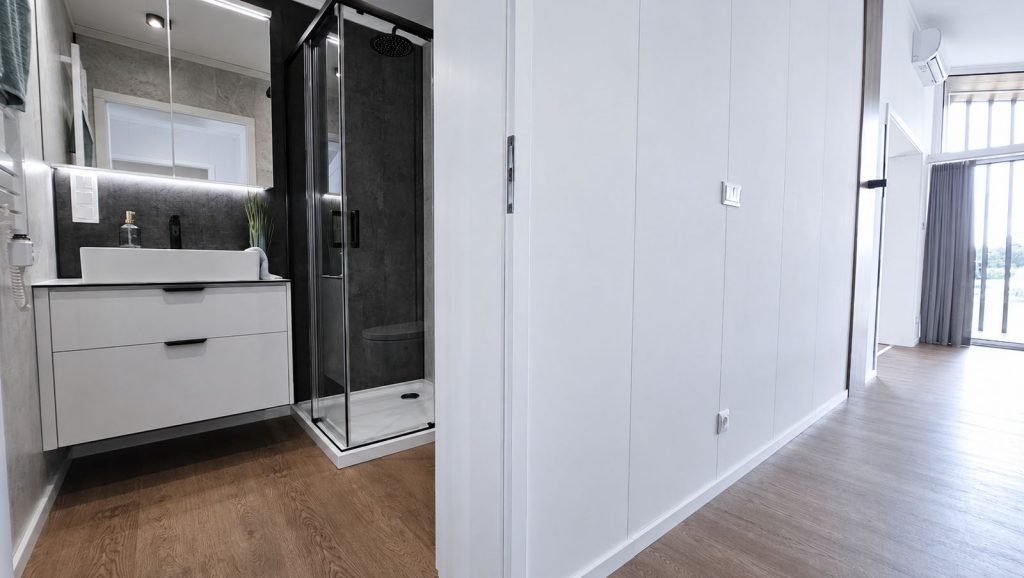Badezimmer mit weissem Waschtisch, dunkler Duschkabine und Steinoptik-Wand, daneben der Flur mit Holzboden - modernes Eigenheim.