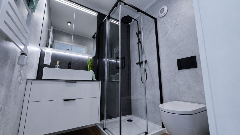 Badezimmer mit Glaseckdusche, Regenbrause und weissem Waschtisch in Steinoptik - Fertigteilhaus fuer Klagenfurt.
