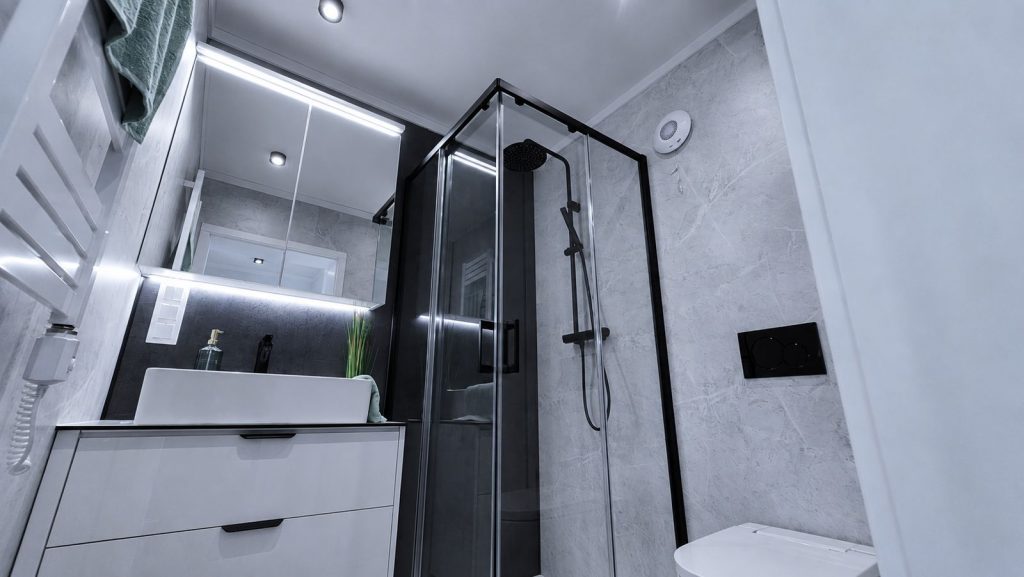 Elegantes Bad mit Eckdusche, Aufsatzwaschbecken und Marmoroptik im stimmungsvoll beleuchteten Fertighaus.