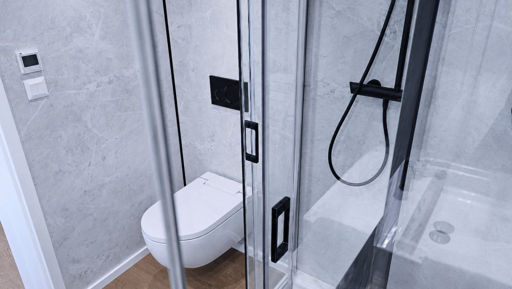 Bad mit grauer Marmoroptik, Haenge-WC mit schwarzer Betaetigungsplatte und Glasdusche mit schwarzen Armaturen - vollmoebliert.