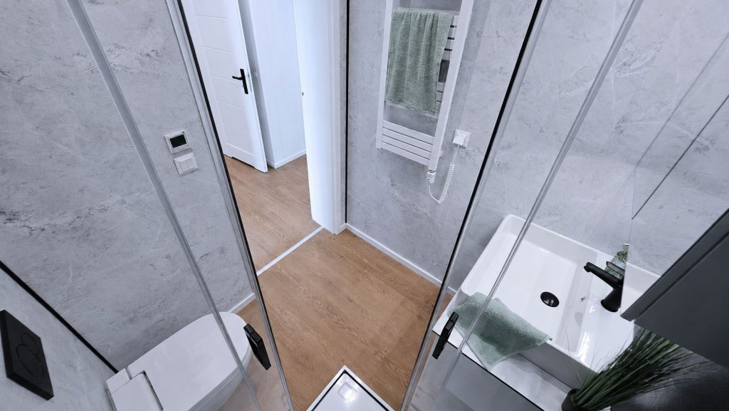 Badezimmer mit Glasdusche, Wand-WC und Waschtisch in Marmoroptik - hochwertige Massivmodul-Architektur.