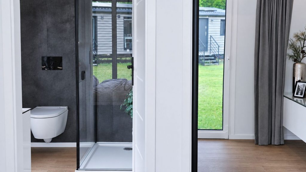 Duschbad mit Wand-WC in dunkler Betonoptik, daneben bodentiefes Fenster zur Wiese - modernes Eigenheim.