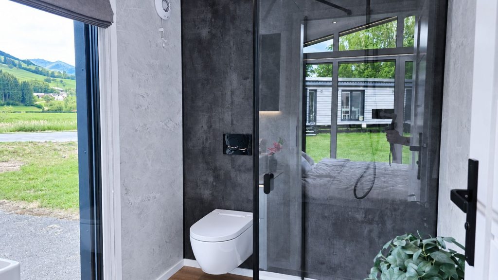Bad mit Beton-Optik, Wand-WC und Glasdusche, Panoramafenster mit Wiesenblick, wohnfertig im Diamond Vario Deluxe.