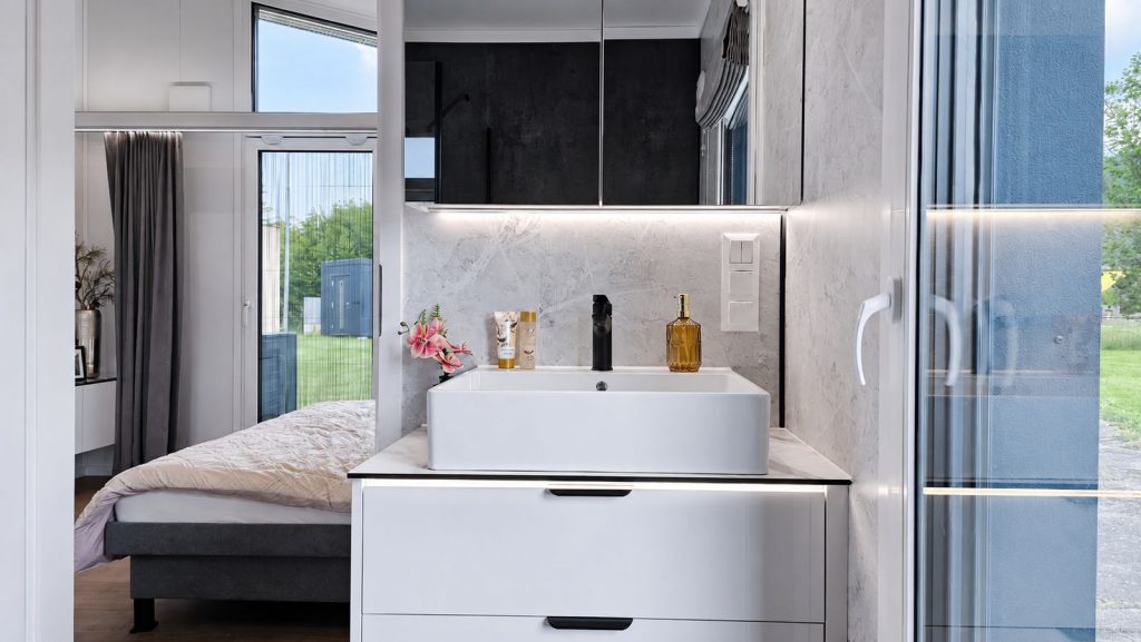 Bad mit Aufsatzwaschbecken, Marmoroptik und Spiegelschrank, Blick ins Schlafzimmer - Modulhaus aus oesterreichischer Fertigung.