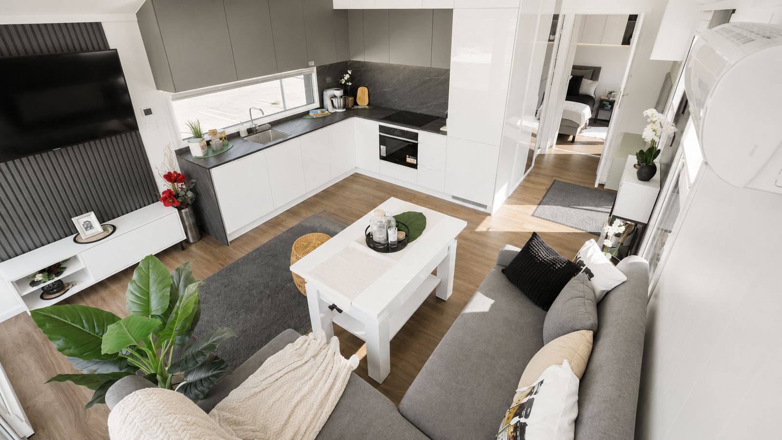 Offener Wohnraum im Diamond XS Deluxe mit L-Kueche, TV-Wand und Sofa - modernes Eigenheim, verfuegbar in Wien.