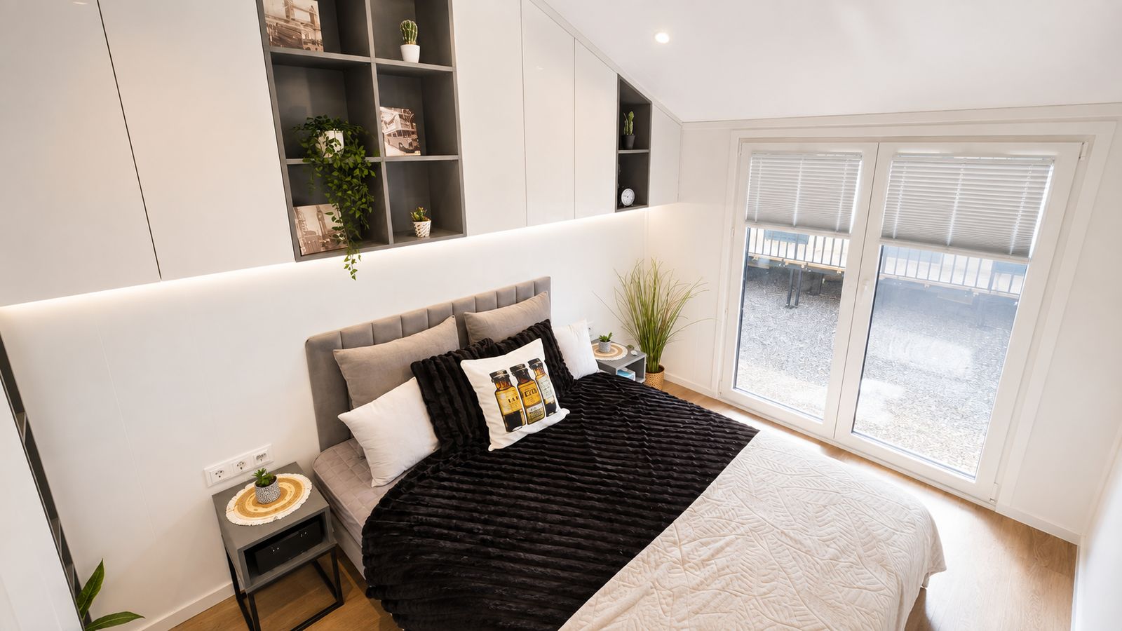 Schlafzimmer mit weissen Einbauschraenken, dunklem Fellueberwurf und bodentiefem Fenster zur Terrasse - wohnfertig eingerichtet.
