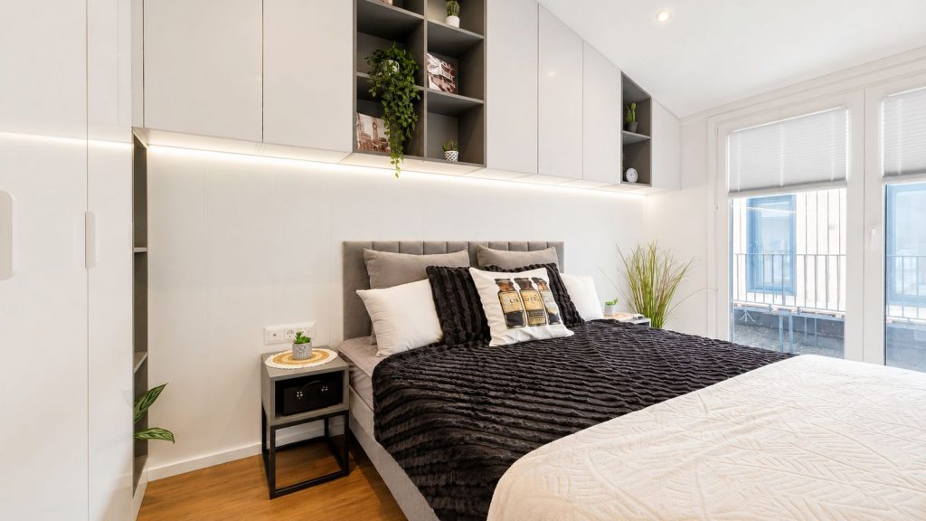 Schlafzimmer mit gepolstertem Kopfteil, viel Stauraum und grossem Balkonfenster - komfortables Ganzjahreshaus.