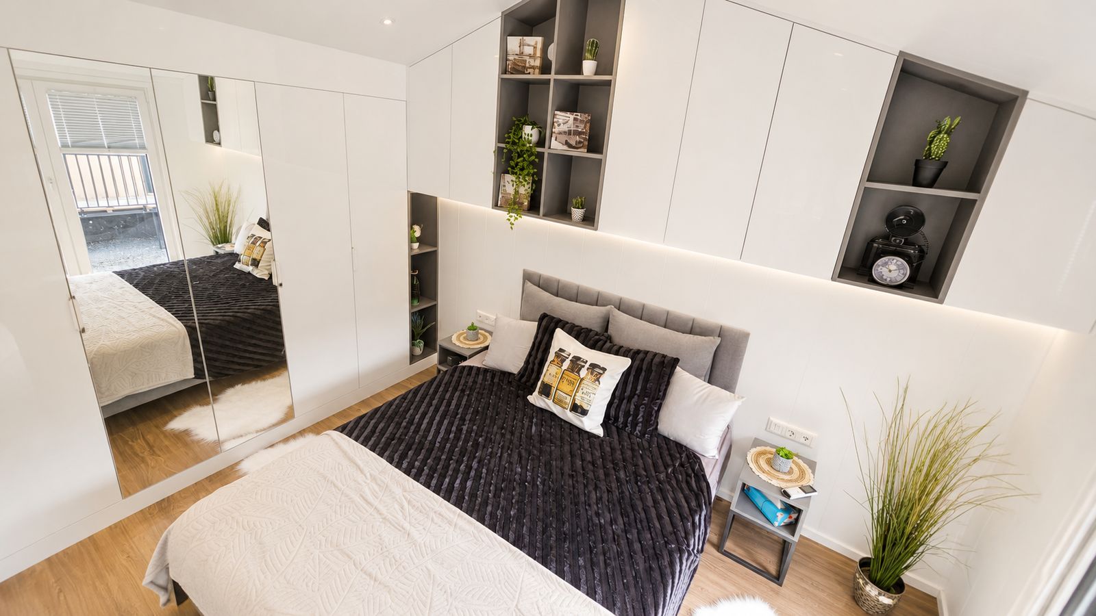 Schlafzimmer mit dunkler Tagesdecke, Spiegelschrank und grauen Regalnischen - durchdachtes Premium-Modulhaus.