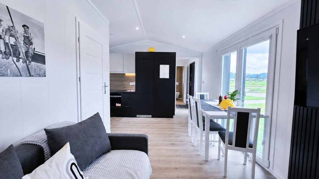 Wohn-Essbereich im Quartier WSW mit grauem Sofa, schwarzer Kuechenzeile und Esstisch - Fertighaus, Lieferung nach Niederoesterreich.