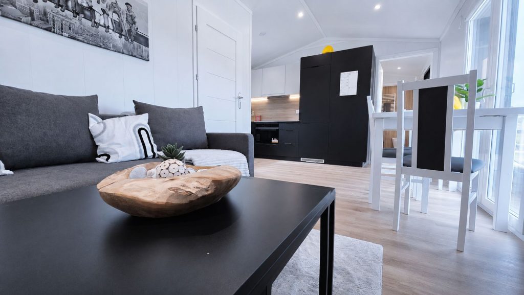 Modernes Eigenheim: Wohnzimmer mit grauem Sofa, schwarzem Couchtisch und offener Kueche - Lieferung nach Graz.