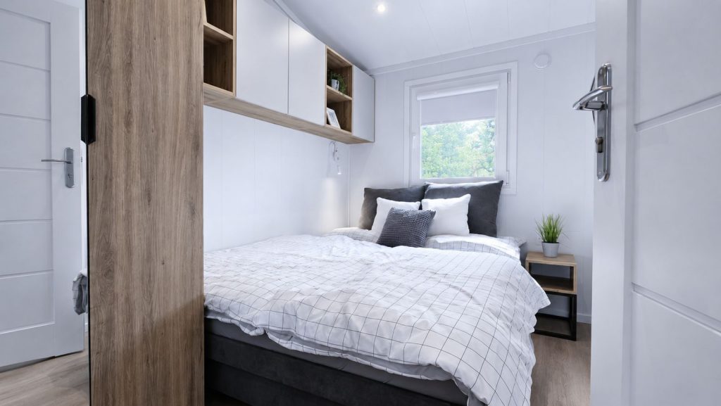 Schlüsselfertiges Schlafzimmer mit Doppelbett, Hängeschränken in Holz-Weiß und Fenster ins Grüne.