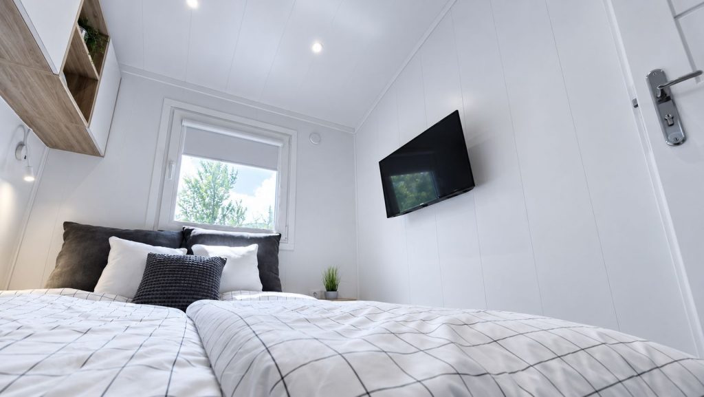 Schlafzimmer mit Doppelbett, karierter Bettwaesche und Wand-TV im Modulhaus - Lieferung nach St. Poelten.