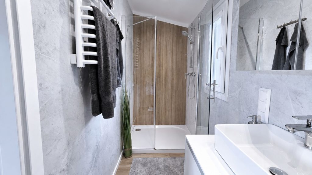 Badezimmer mit Marmoroptik-Waenden, Duschkabine mit Holzrueckwand und weisser Handtuchheizung - modernes Eigenheim.