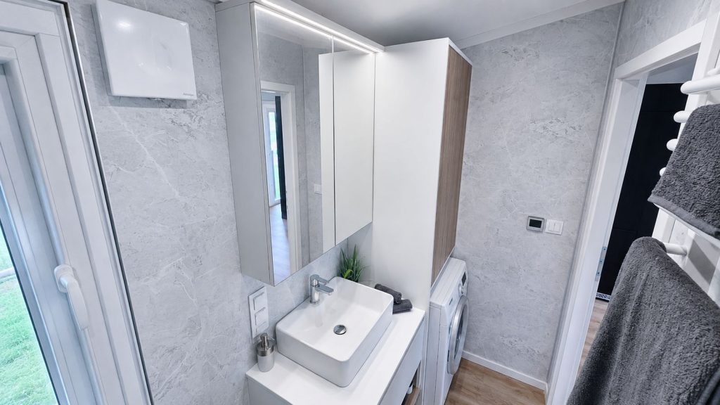 Badezimmer mit grauer Marmoroptik, Spiegelschrank, Aufsatzwaschbecken und integrierter Waschmaschine - Premium-Modulhaus von BOND.