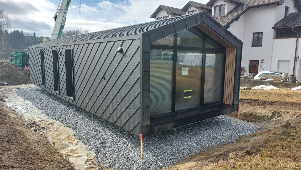 Premium-Modulhaus ATB 39 mit verglaster Giebelfront und warmen Holzleibungen, aufgestellt auf Schotterbett.