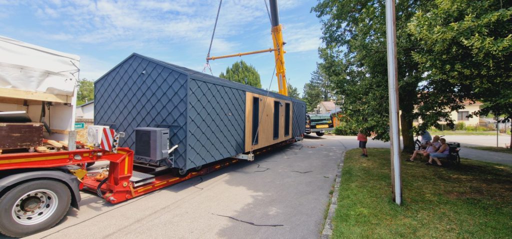 Seitenansicht des BOND-Fertighauses mit Rautenfassade und Holzelement auf dem Transportanhänger.