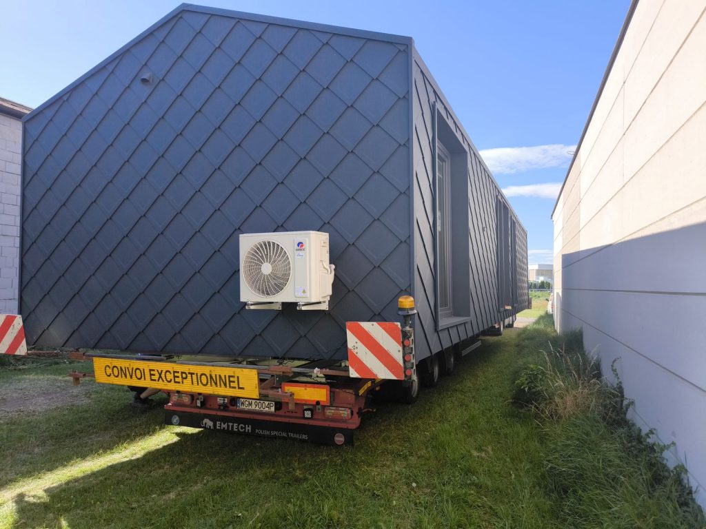 Das ATB 53 mit dunkler Rautenfassade und Klimagerät wird zwischen zwei Gebäuden zum Standort manövriert.