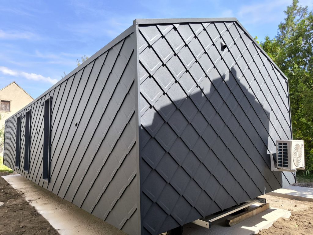 Untersicht der anthrazitfarbenen Metall-Rautenfassade des ATB 53 mit Klimagerät im Sonnenlicht.