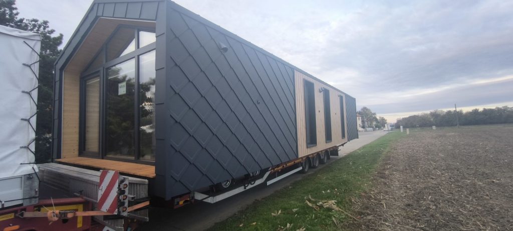 Modulhaus ATB 55 mit anthrazitfarbener Rautenfassade und verglaster Giebelfront auf dem Tieflader bei der Anlieferung.