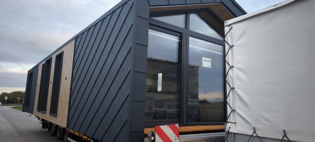 Verglaste Giebelfront des Premium-Modulhauses ATB 55 mit warmer Holzuntersicht und Sitzbank aus Holz.