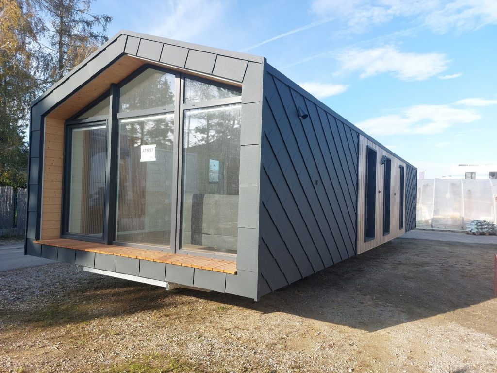 Premium-Modulhaus ATB 57 im Freien, verglaste Giebelfront, Holzterrasse und anthrazitgraue Rautenfassade.