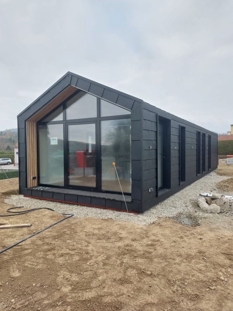 Schwarzes Premium-Modulhaus ATB 58 mit verglaster Giebelfront, Holzakzent und Terrassendeck auf dem Grundstück.