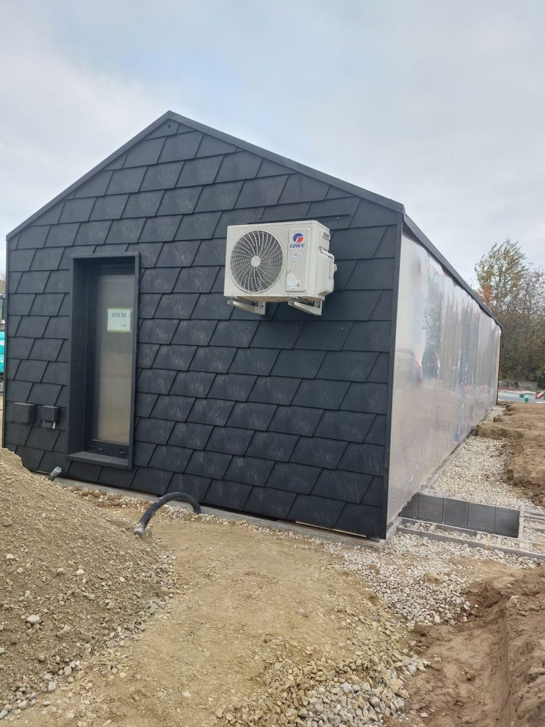 Giebeldetail des schwarzen Modulhauses ATB 58 mit Wärmepumpe und schmalem, hohem Fensterelement.