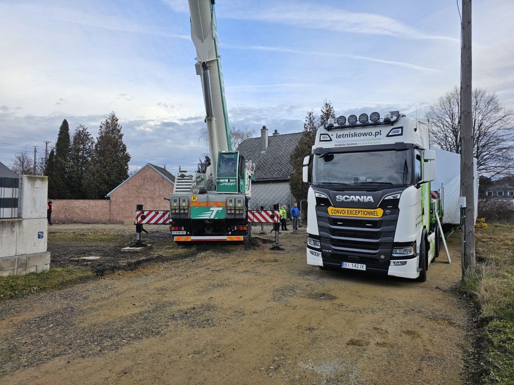 Weißer Scania-Sattelzug und Mobilkran liefern ein BOND-Modulhaus an den Aufstellort.