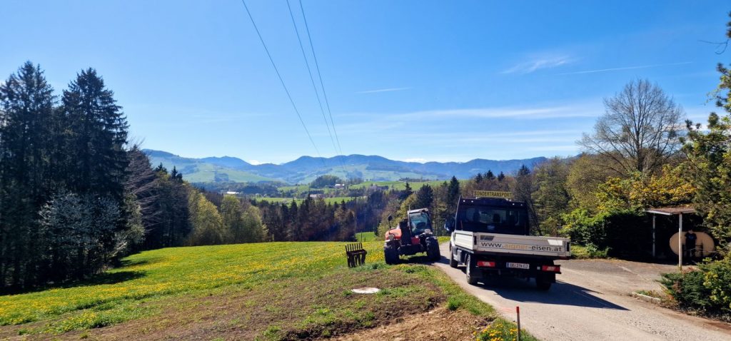 Sondertransport über einen Feldweg mit blühender Löwenzahnwiese und Bergpanorama im Hintergrund