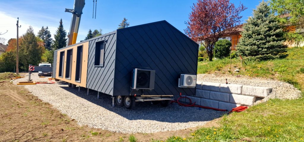 Auf Schraubfundament und Schotterbett platziertes Modulhaus mit Rautenfassade neben einer Natursteinmauer