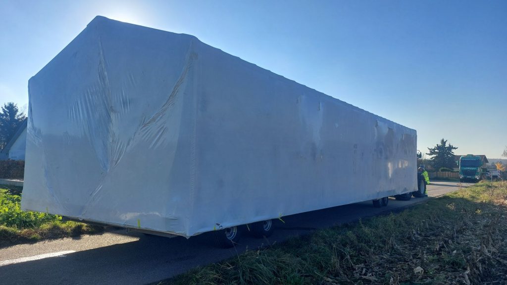 Foliengeschütztes BOND-Modulhaus ATB 67 auf dem Tieflader bei der Anlieferung im Morgenlicht.