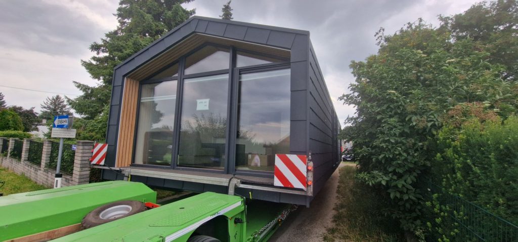 BOND Modulhaus mit Panoramafenster und anthrazitfarbener Rautenschindel-Fassade auf dem Tieflader beim Transport.