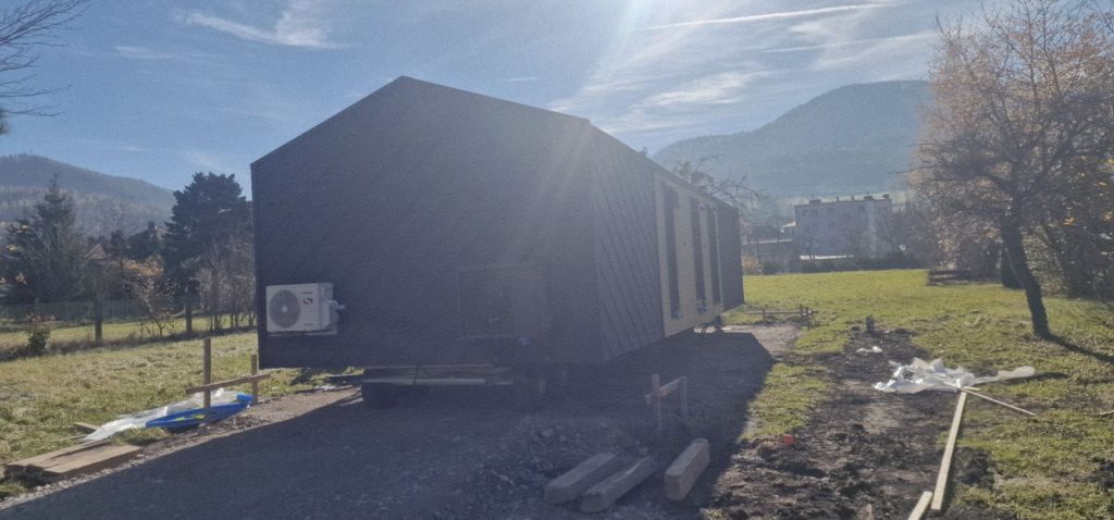 Dunkles Modul im Gegenlicht vor Bergpanorama mit Außengerät der Wärmepumpe an der Fassade