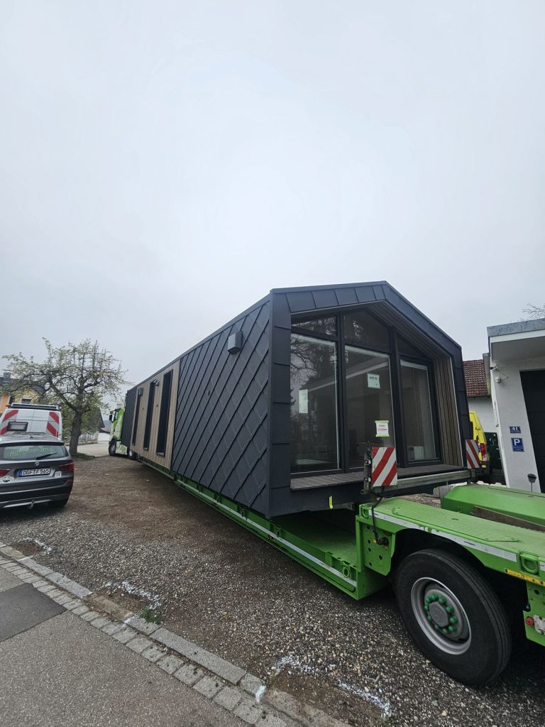 BOND Modulhaus ATB 71 mit Panoramaverglasung und anthrazitfarbener Rautenfassade beim Transport auf dem Tieflader.