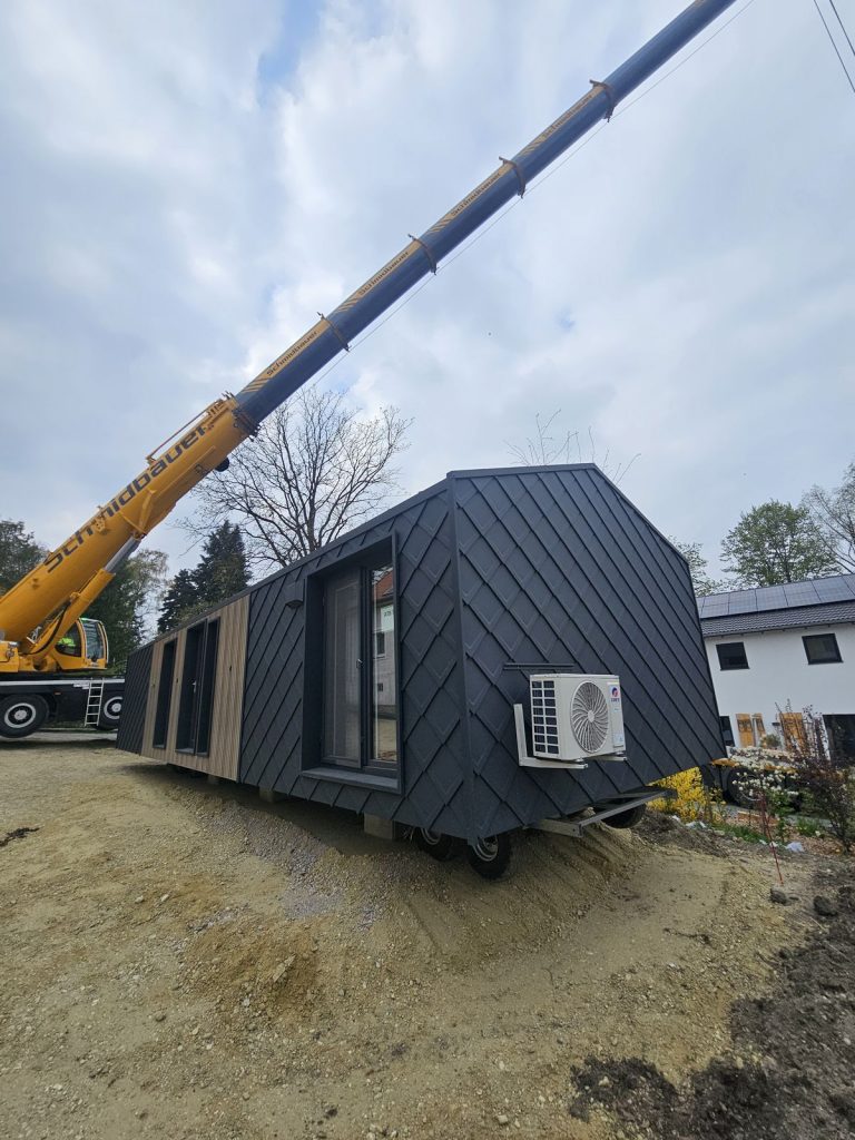 Seitenansicht des ATB 71 mit Holzfassade, Eingangstür und Klimaeinheit während der Positionierung per Kran.