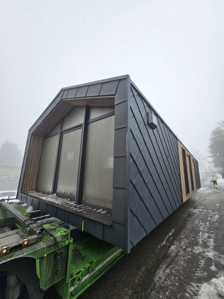 Bodentiefe Panoramaverglasung an der holzgerahmten Giebelseite des Modulhauses ATB 76 während des Transports.