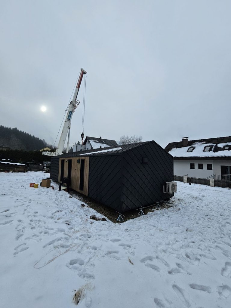 Modulhaus ATB 76 auf Punktfundamenten mit holzverkleideter Eingangsseite und Doppeltür im Schnee.