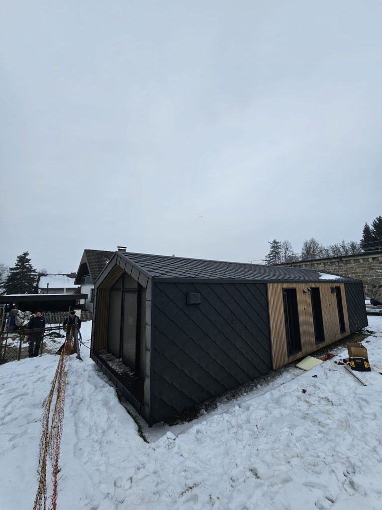 Dach- und Längsansicht des ATB 76 mit anthrazitfarbenem Rautendach und drei Fenstern in der warmen Holzfassade.