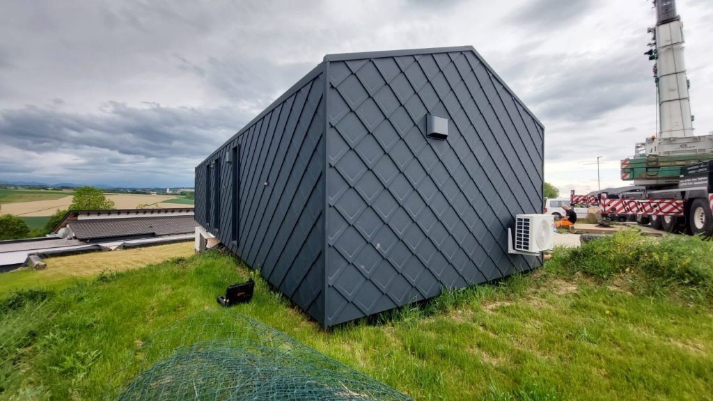 BOND Modulhaus auf der Wiese mit weitem Blick über Felder und Hügel, Rautenfassade in Anthrazit