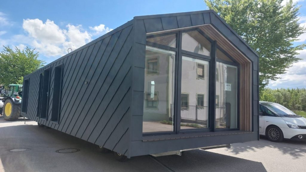 Giebelfront des BOND Modulhauses mit großem Panoramafenster und Holzakzent bei sonnigem Himmel