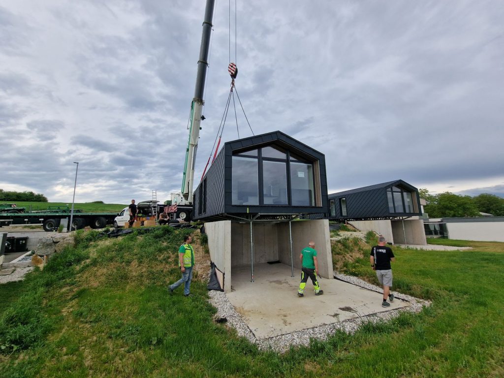 Baustelle mit Kran und zwei dunklen Modulen eines Ganzjahreshauses über offenem Betonunterbau