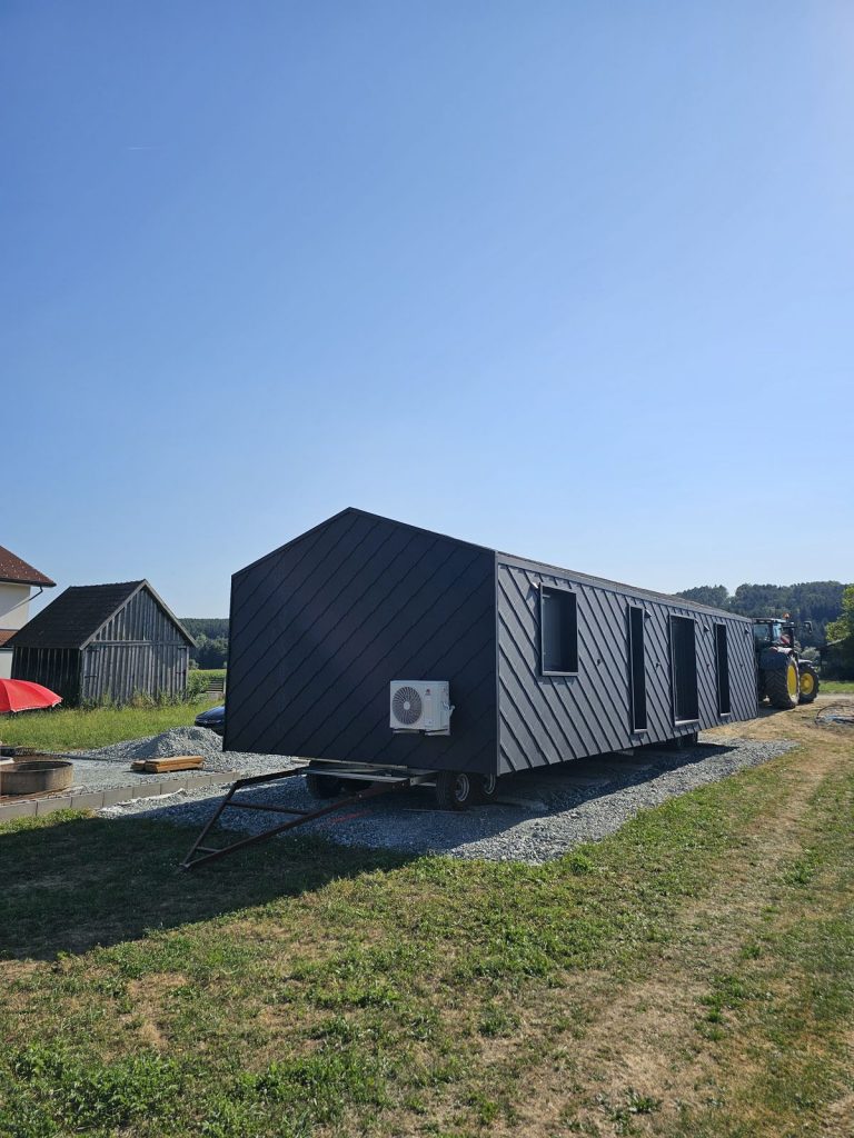 Anthrazitfarbenes BOND-Modulhaus mit rautenförmiger Metallfassade auf dem Transportfahrgestell in Pilgersdorf.