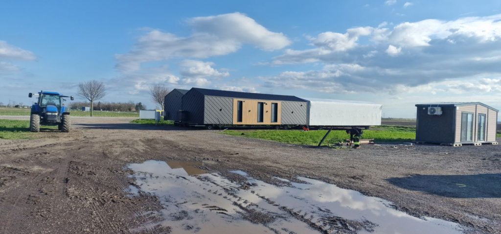 Modulhaus ATB 41 am Gelände in Raasdorf, daneben ein Traktor und ein foliertes Modul unter blauem Himmel.