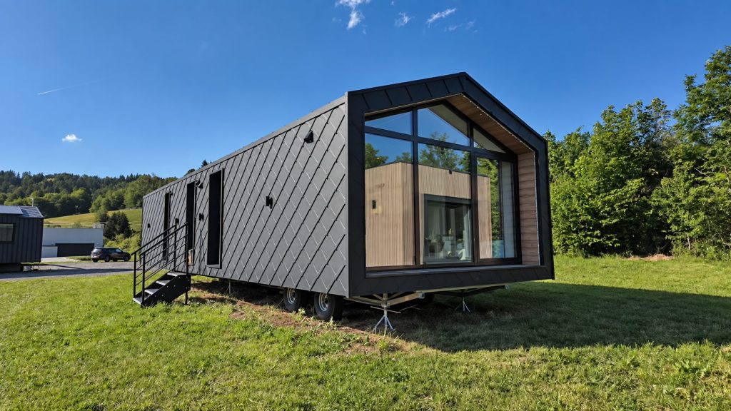 Schwarzes Modulhaus Diamond +Plus ATB-38 mit PREFA-Rautenfassade und verglaster Giebelseite auf einer Wiese.