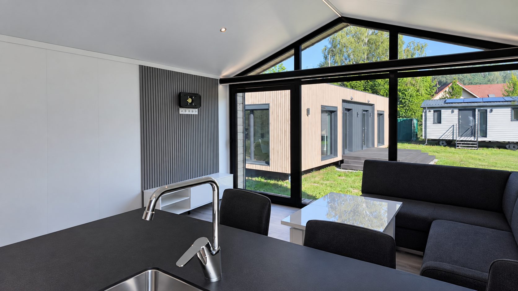 Offene Wohnküche im Modulhaus Diamond +Plus ATB-38 mit Kücheninsel, Sofa und Giebelverglasung.