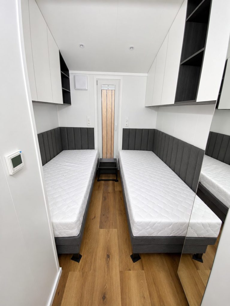 Gästezimmer im Modulhaus Diamond +Plus Deluxe ATB-62 mit gepolsterten Wandpaneelen und Einbauschränken.