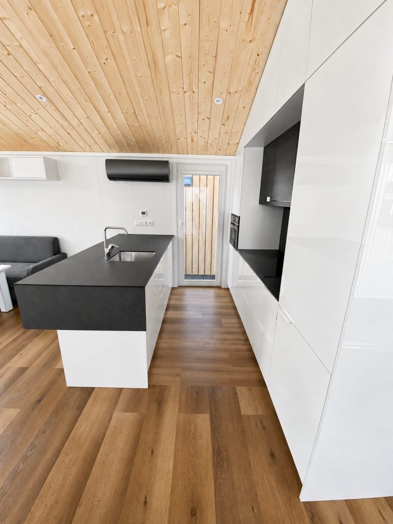 Küche des Diamond +Plus Deluxe ATB-62 mit weißen Hochglanzfronten, dunkler Nische und Kücheninsel.